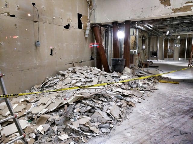 Interior demolition site with drywall debris and caution tape